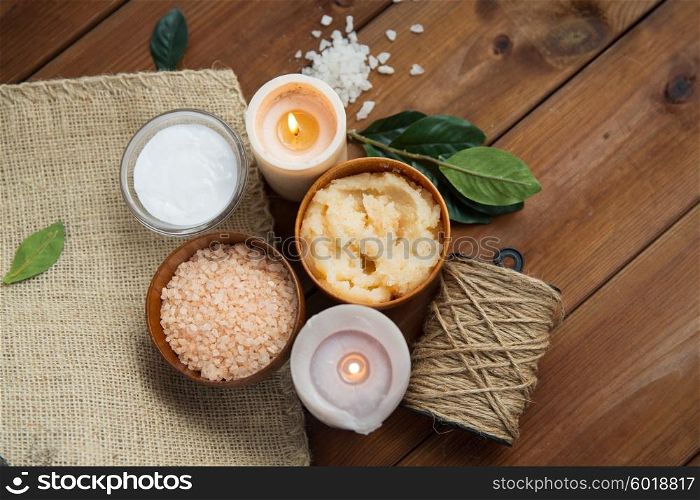 beauty, spa, therapy, natural cosmetics and wellness concept - close up of body scrub with himalayan pink salt and candles on wood