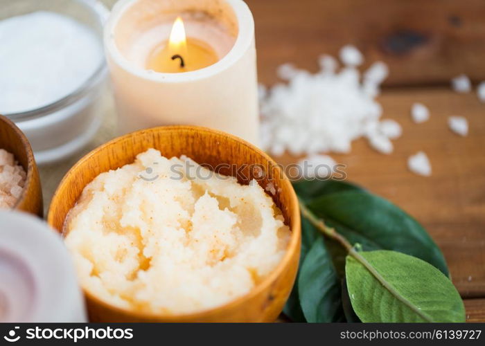 beauty, spa, therapy, natural cosmetics and wellness concept - close up of body scrub and candle on wood