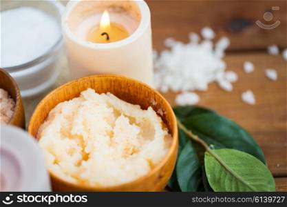beauty, spa, therapy, natural cosmetics and wellness concept - close up of body scrub and candle on wood