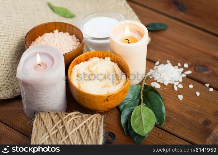 beauty, spa, therapy, natural cosmetics and wellness concept - close up of body scrub with himalayan pink salt and candles on wood