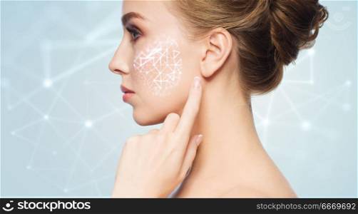 beauty, technology and people concept - beautiful young woman pointing finger to her skin over blue background with low poly shape projection on cheek. beautiful woman with low poly projection on cheek. beautiful woman with low poly projection on cheek