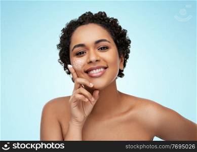 beauty, technology and people concept - happy smiling young african american woman with moisturizer on her finger tip and low poly shape projection on her face over blue background. young african american woman with moisturizer