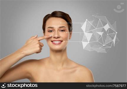 beauty, technology and science concept - smiling beautiful young woman showing her face and pointers with low poly shape projection over grey background. beautiful woman pointing finger to face skin
