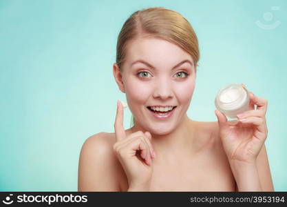 Beauty treatment. Woman applying moisturizing cream on face, holding jar with skin care product, studio shot on green blue background