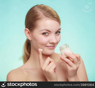 Beauty treatment. Woman applying moisturizing cream on face, holding jar with skin care product, studio shot on green blue background. woman applying cream on her skin face.