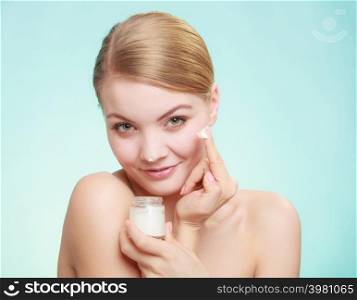 Beauty treatment. Woman applying moisturizing cream on face, holding jar with skin care product, studio shot on green blue background. woman applying cream on her skin face.