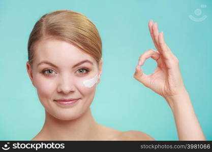 Beauty treatment. Woman applying moisturizing cream skin care product on face, making ok sign studio shot on green blue background. woman applying cream on her skin face.
