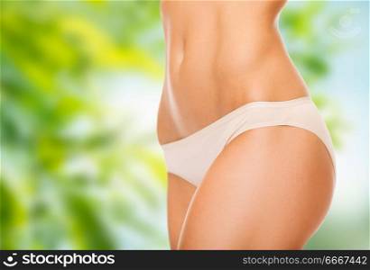 beauty, underwear and slimming concept - close up of woman body in cotton pants over green natural background. close up of woman body in cotton underwear. close up of woman body in cotton underwear