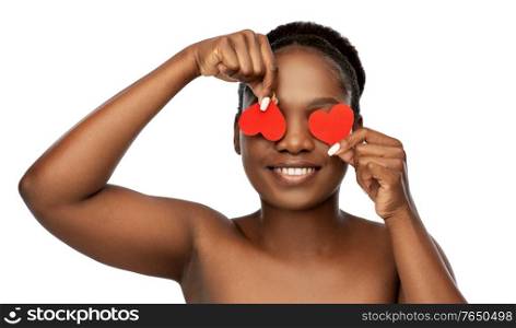 beauty, valentine&rsquo;s day and people concept - portrait of happy smiling young african american woman with bare shoulders with red hearts covering her eyes over white background. smiling african american woman with red hearts