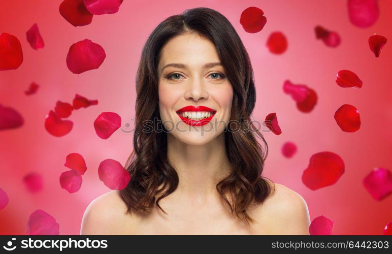 beauty, valentines day, make up and people concept - happy smiling young woman with red lipstick over rose petals on background. beautiful smiling young woman with red lipstick