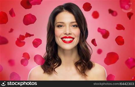 beauty, valentines day, make up and people concept - happy smiling young woman with red lipstick over rose petals on background. beautiful smiling young woman with red lipstick