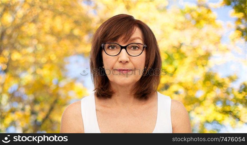 beauty, vision and old people concept - portrait of senior woman in glasses over natural autumn background. portrait of senior woman in glasses over autumn