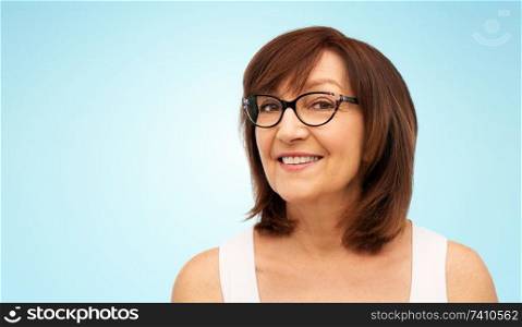 beauty, vision and old people concept - portrait of smiling senior woman in glasses over blue background. portrait of senior woman in glasses over blue
