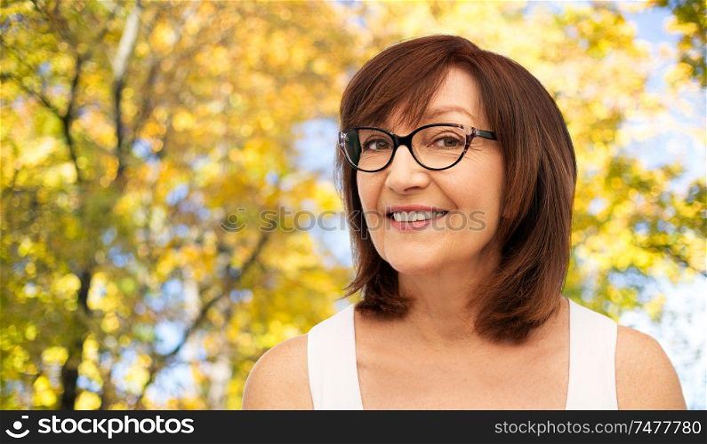 beauty, vision and old people concept - portrait of smiling senior woman in glasses over natural autumn background. portrait of senior woman in glasses in autumn