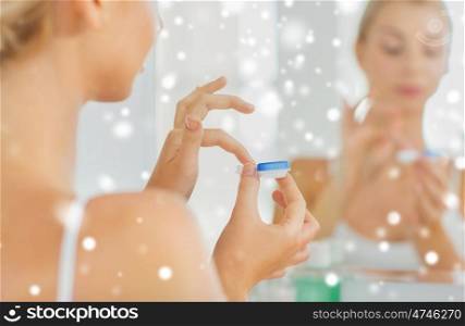 beauty, vision, eyesight, ophthalmology and people concept - close up of young woman applying contact lenses at mirror in home bathroom over snow