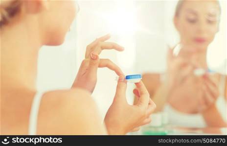 beauty, vision, eyesight, ophthalmology and people concept - close up of young woman applying contact lenses at mirror in home bathroom. young woman applying contact lenses at bathroom. young woman applying contact lenses at bathroom