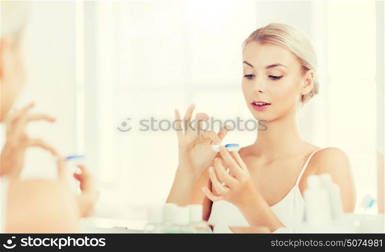 beauty, vision, eyesight, ophthalmology and people concept - young woman putting on contact lenses at mirror in home bathroom. young woman putting on contact lenses at bathroom