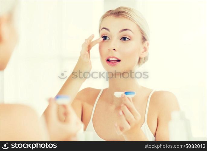 beauty, vision, eyesight, ophthalmology and people concept - young woman putting on contact lenses at mirror in home bathroom. young woman putting on contact lenses at bathroom