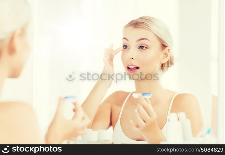 beauty, vision, eyesight, ophthalmology and people concept - young woman putting on contact lenses at mirror in home bathroom. young woman putting on contact lenses at bathroom. young woman putting on contact lenses at bathroom