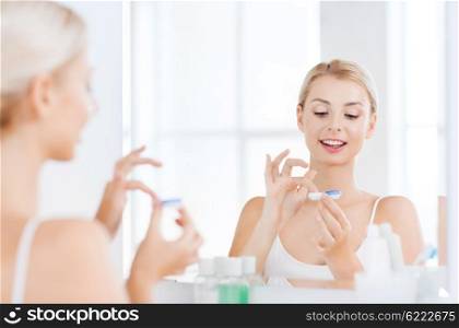 beauty, vision, eyesight, ophthalmology and people concept - young woman putting on contact lenses at mirror in home bathroom