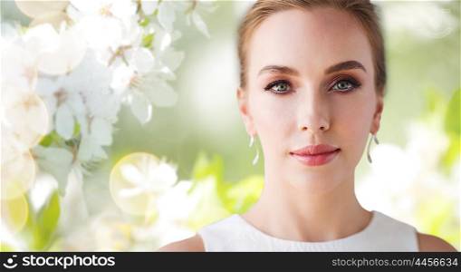 beauty, wedding and people concept - face of beautiful woman or bride in white dress over natural spring cherry blossom background