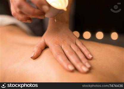 beauty, wellness and bodycare concept - close up of woman having back massage with hot oil candle at spa. back massage with hot oil candle at spa