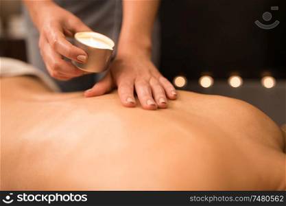 beauty, wellness and bodycare concept - close up of woman having back massage with hot oil candle at spa. back massage with hot oil candle at spa