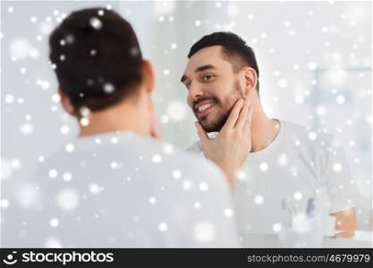 beauty, winter, christmas and people concept - smiling young man looking to mirror at home bathroom over snow