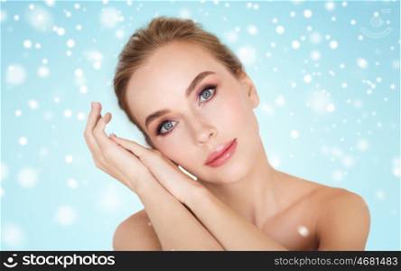 beauty, winter, people and bodycare concept - beautiful young woman face and hands over blue background and snow