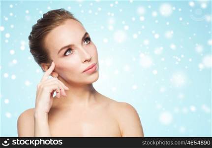 beauty, winter, people and health concept - beautiful young woman touching her face over blue background and snow
