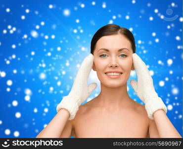 beauty, winter, people and health concept - smiling young woman in white mittens over blue snowy background