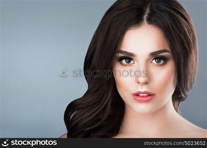 Beauty woman portrait. Beautiful woman with long wavy brown hair. Closeup beauty portrait of a fashion model posing at studio on gray background
