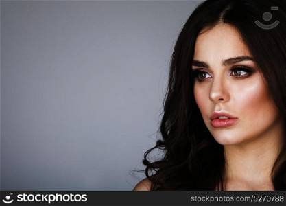 Beauty woman portrait. Beautiful woman with long wavy brown hair. Closeup beauty portrait of a fashion model posing at studio on gray background