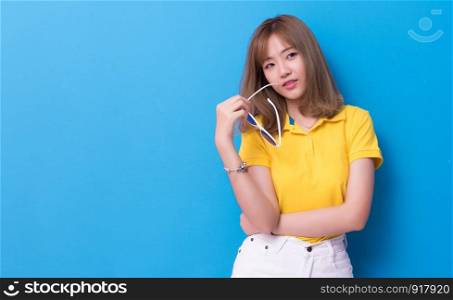 Beauty woman posing with sunglasses in front of blue wall background. Summer and vintage concept. Happiness lifestyle and people portrait theme. Cute and pastel tone.