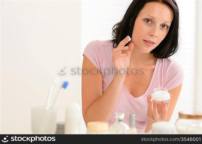 Beauty woman putting facial cream in front of bathroom mirror