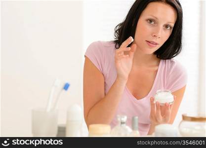 Beauty woman putting facial cream in front of bathroom mirror