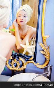 Beauty woman with towel looking at golden mirror putting cream