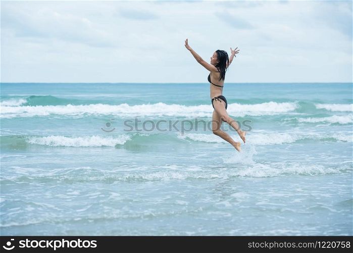 beauty women girl black hair with brown swimsuit bikini jumping on a beach and wave sea