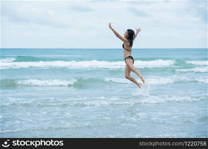 beauty women girl black hair with brown swimsuit bikini jumping on a beach and wave sea