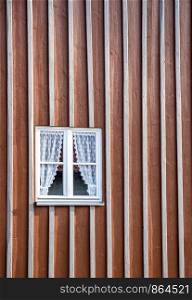 Beauty wooden window with curtains in a house facade wall.