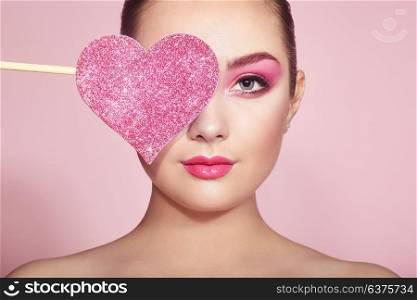 Beauty Young Fashion model Girl with Symbol Valentine Heart shaped in hand. Love. Beautiful young Woman with Holiday Makeup. Valentines Day gift