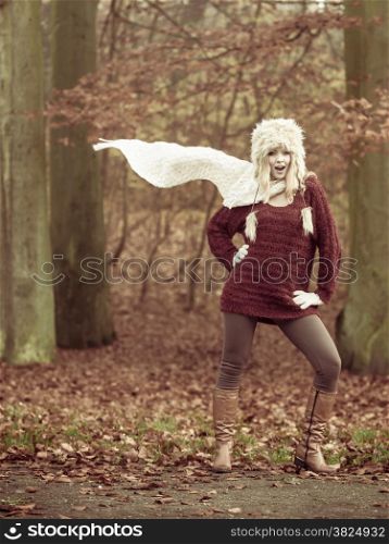 Beauty young woman fashion girl wearing fur cap sweater relaxing posing in autumn park, breathing fresh air, wind blowing scarf outdoor