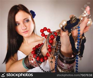 Beauty young woman in summer style with plenty of jewellery, beads in hands gray background
