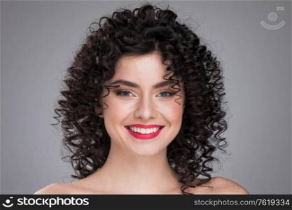 Beauty young woman portrait on gray background. Girl with black curly hair. Hairstyle. Haircut. Model girl with curly hair