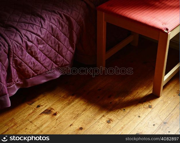 Bed covered with purple bedspread and alongside old retro chair - gloomy and loneliness