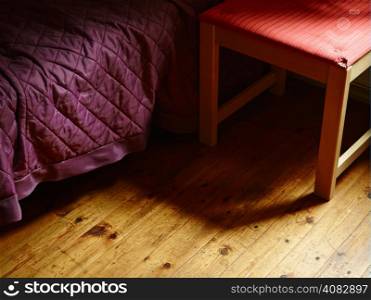 Bed covered with purple bedspread and alongside old retro chair - gloomy and loneliness