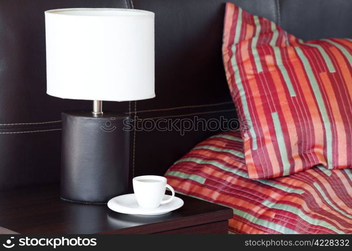 bed with a pillow, a cup of tea on the bedside table and lamp