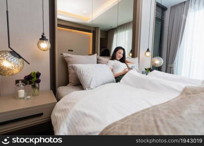 Bedroom concept a girl with drowsy feeling laying her back on several big and comfortable pillows on the bed looking on the mobile screen for social media.