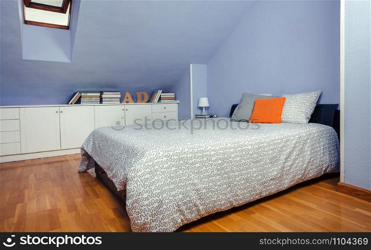 Bedroom in an attic with double bed and chest of drawers with books