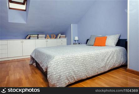 Bedroom in an attic with double bed and chest of drawers with books